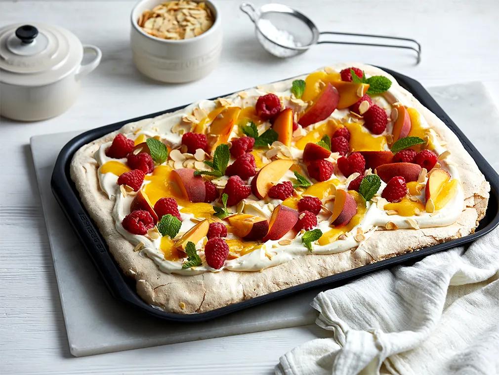 Pavlova vom Blech mit Pfirsichsauce, Himbeeren und Mandelblättchen